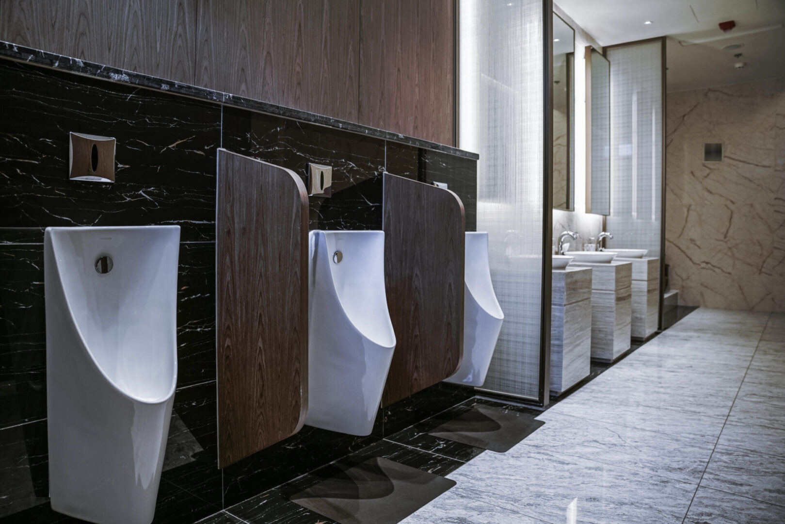 A row of urinals in a bathroom with marble walls.