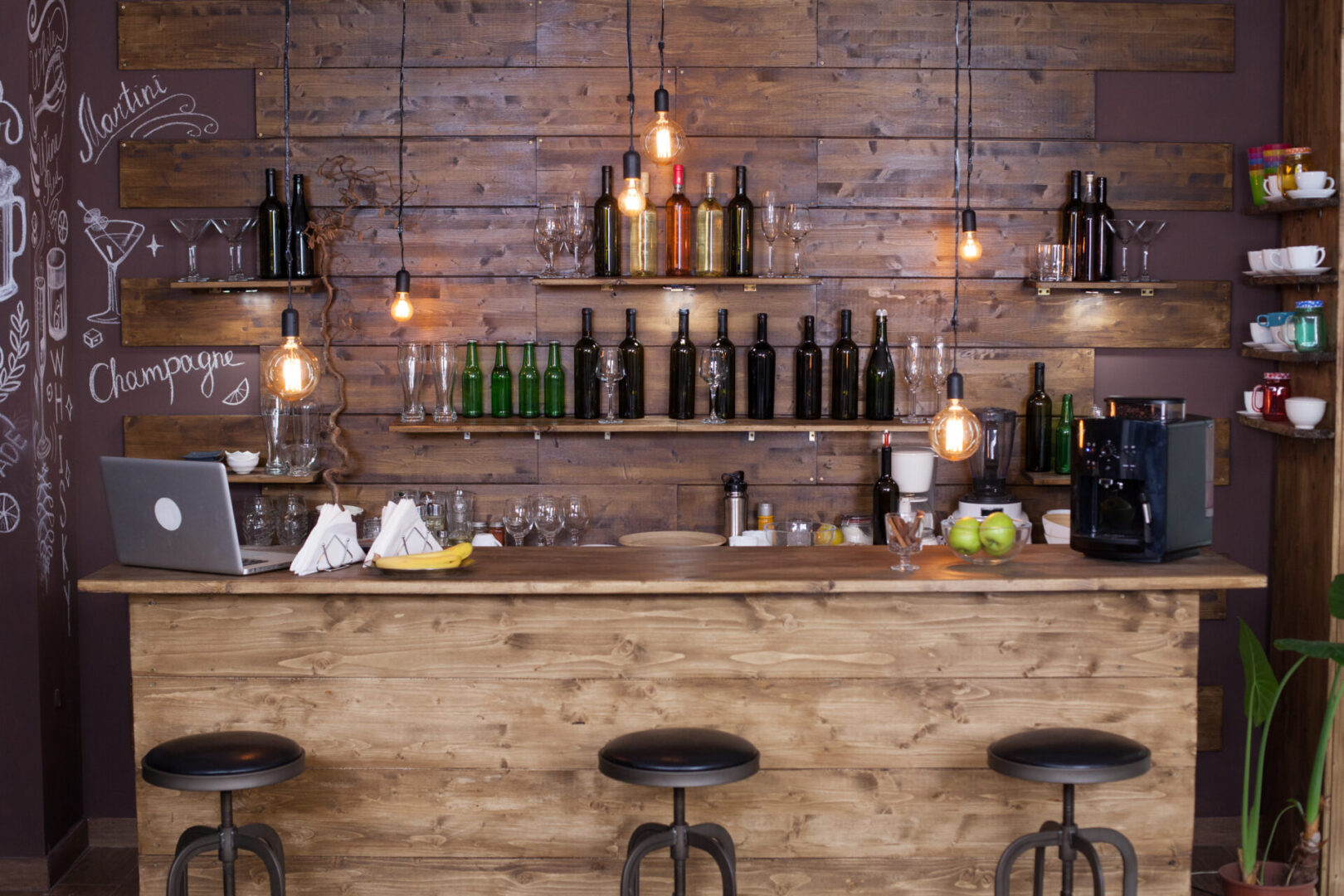 A bar with three stools and bottles on the wall.