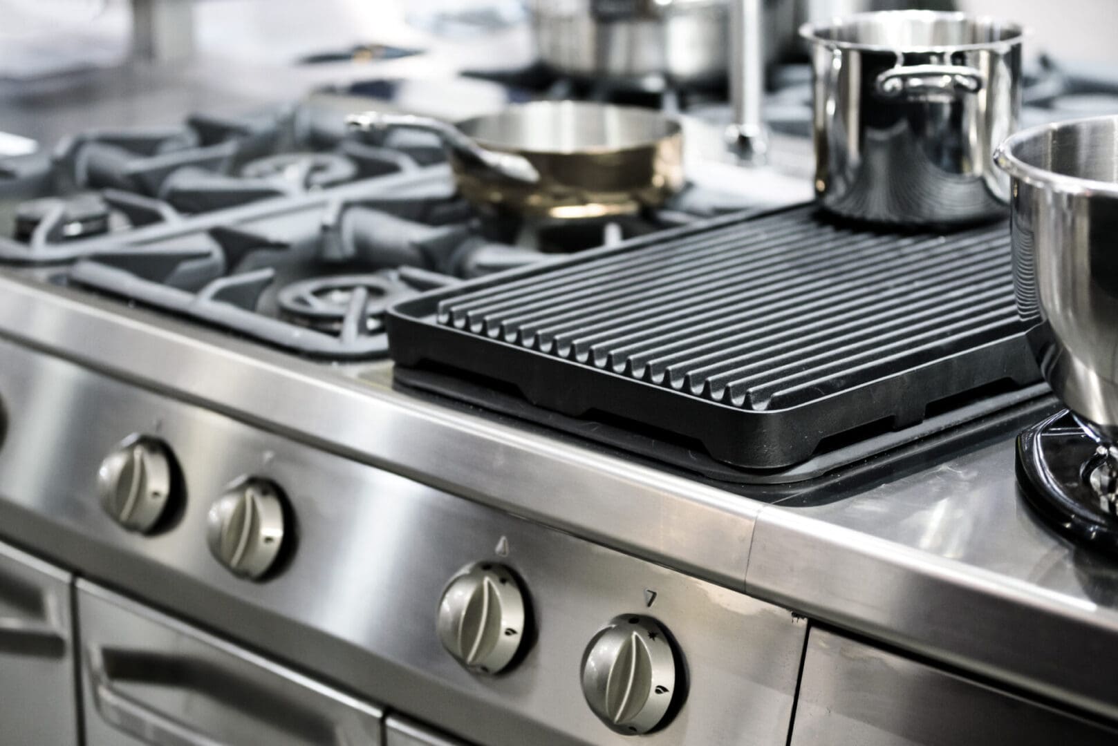 A grill on top of an oven with pots and pans.