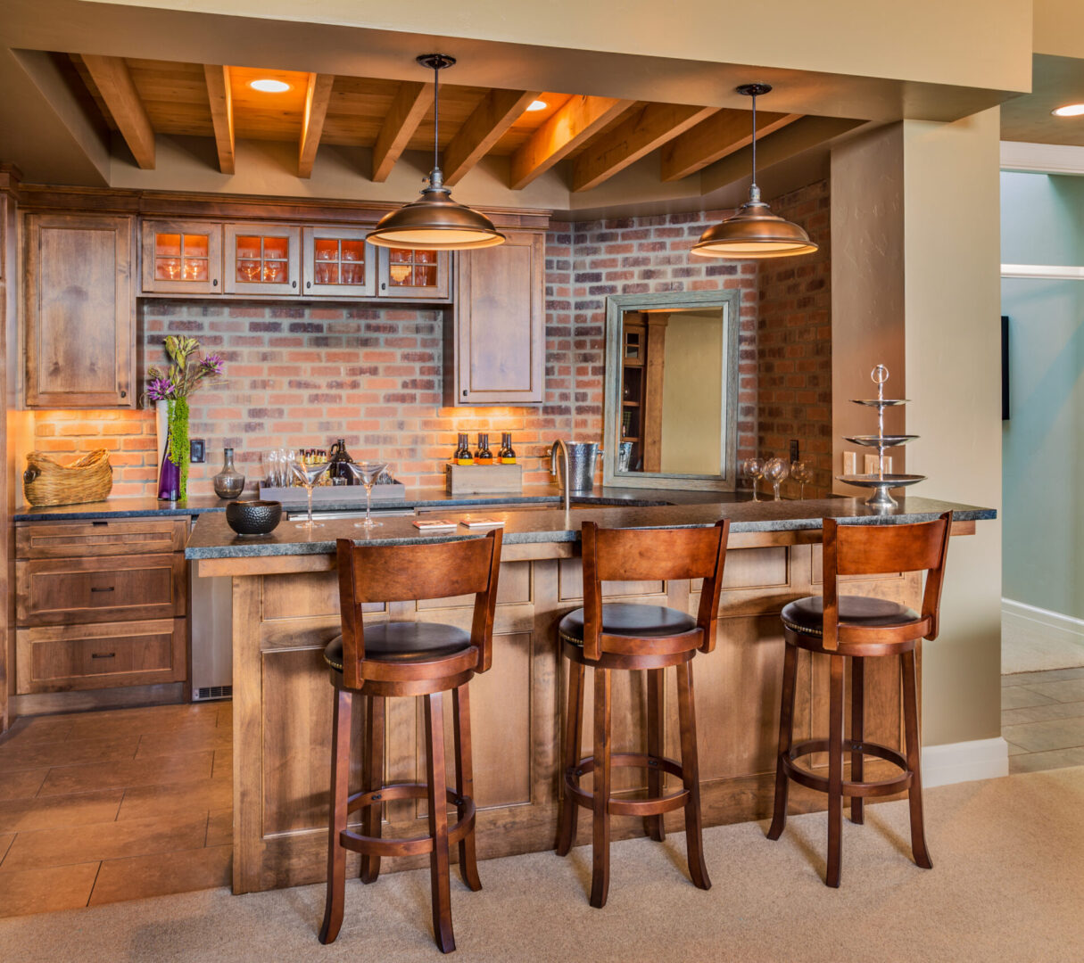 A kitchen with three bar stools and a brick wall.
