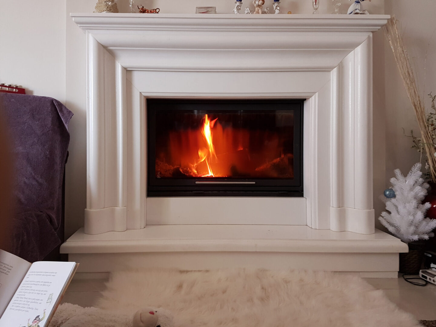 A fireplace with white stone surround and fire burning.
