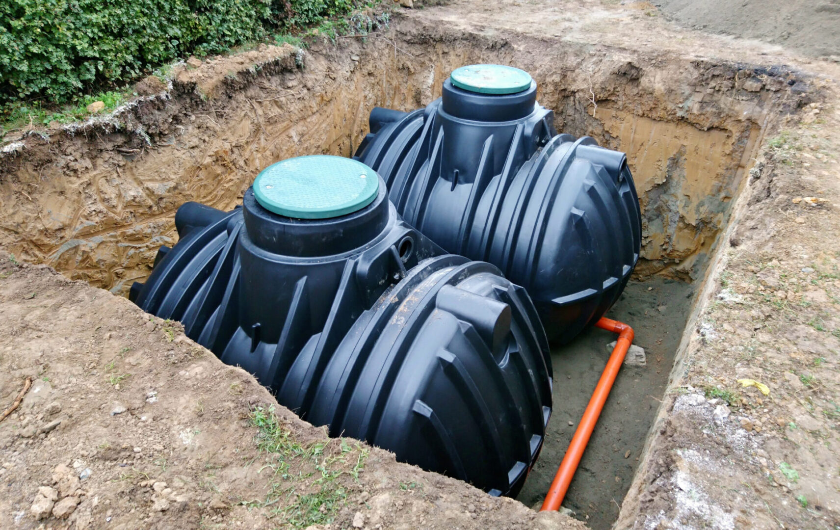 Two black septic tanks in a hole with pipes.