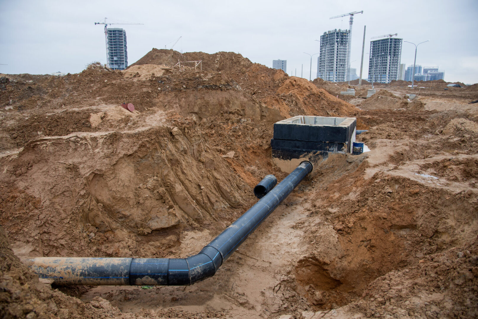 A large pipe is in the dirt near some buildings.