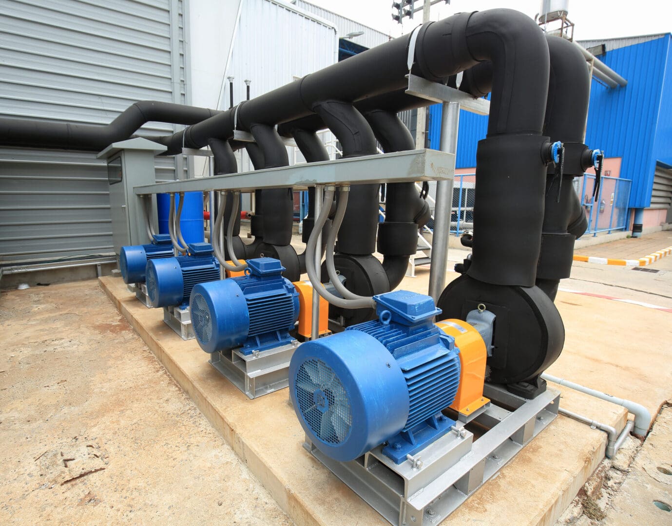 A group of blue and yellow pumps sitting next to black pipes.