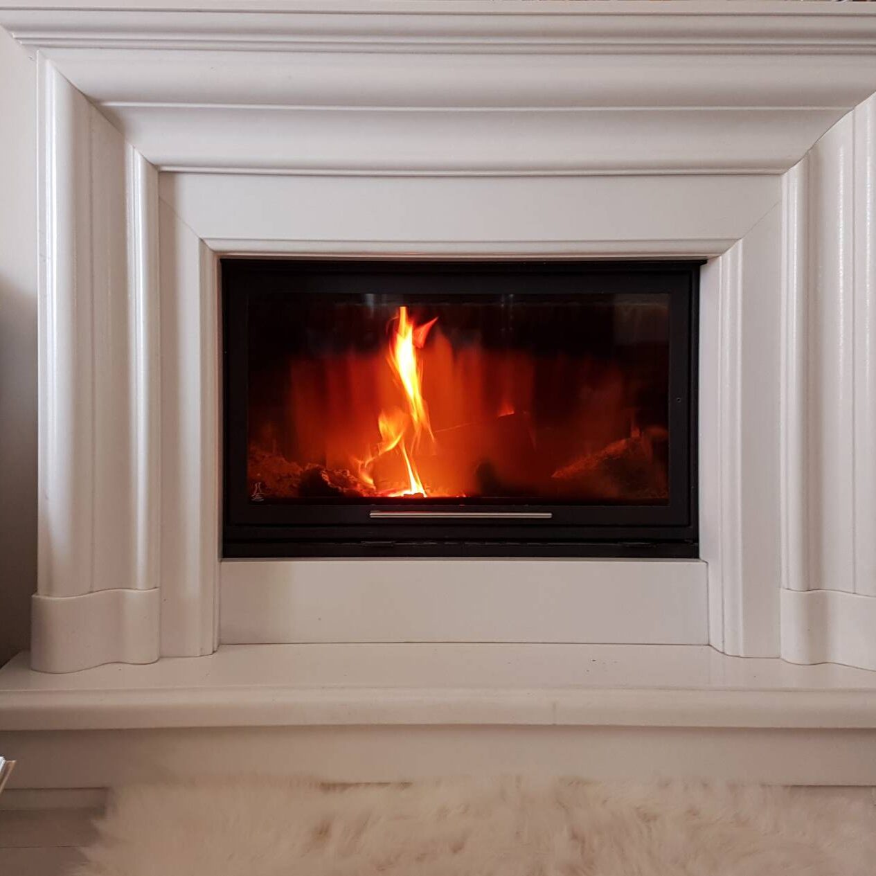 A fire burning in the fireplace of a white room.
